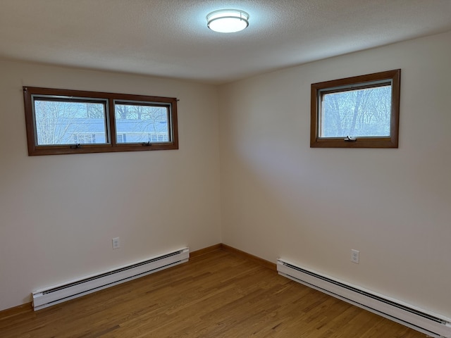 empty room with a baseboard heating unit, baseboards, light wood-style floors, and a textured ceiling