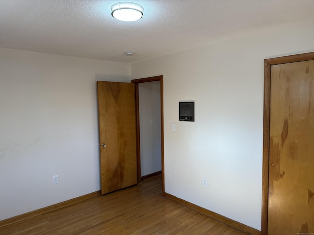 empty room with a textured ceiling, light wood-type flooring, and baseboards