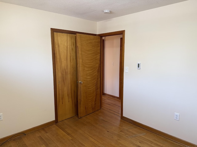 unfurnished bedroom with light wood-style flooring, baseboards, a closet, and a textured ceiling