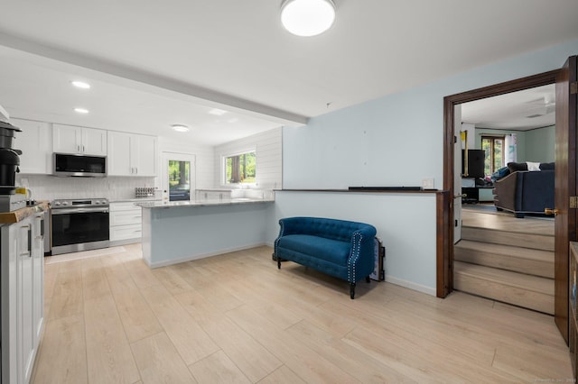 kitchen with appliances with stainless steel finishes, a wealth of natural light, white cabinetry, decorative backsplash, and kitchen peninsula