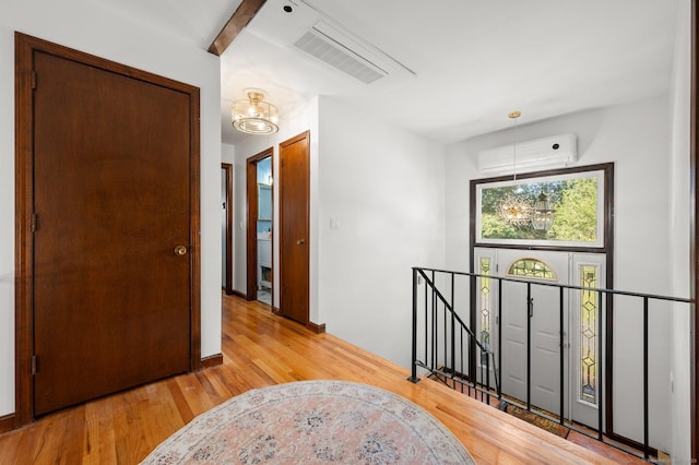 corridor with beam ceiling, a chandelier, light hardwood / wood-style floors, and an AC wall unit