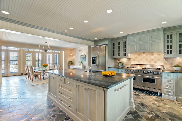 kitchen featuring sink, tasteful backsplash, hanging light fixtures, appliances with stainless steel finishes, and a kitchen island with sink