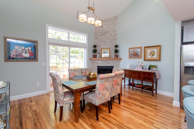 dining space featuring a chandelier, a fireplace, light hardwood / wood-style floors, and high vaulted ceiling