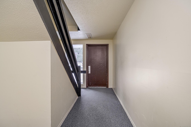 hall featuring dark carpet and a textured ceiling