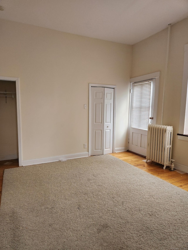 unfurnished bedroom with radiator heating unit, wood finished floors, and baseboards