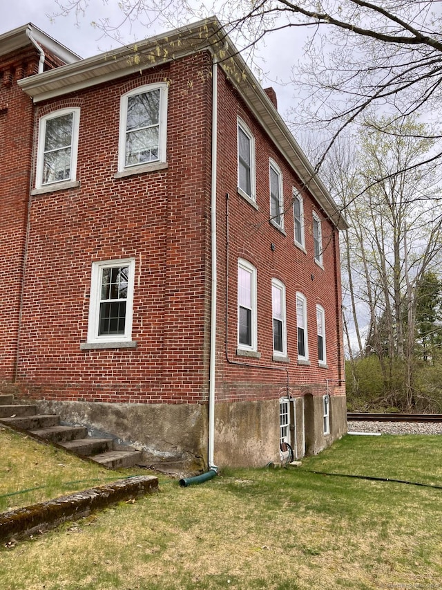 view of home's exterior with a yard, a chimney, and brick siding