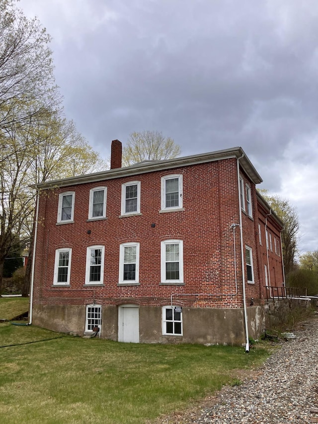 view of side of property featuring a chimney, brick siding, and a yard
