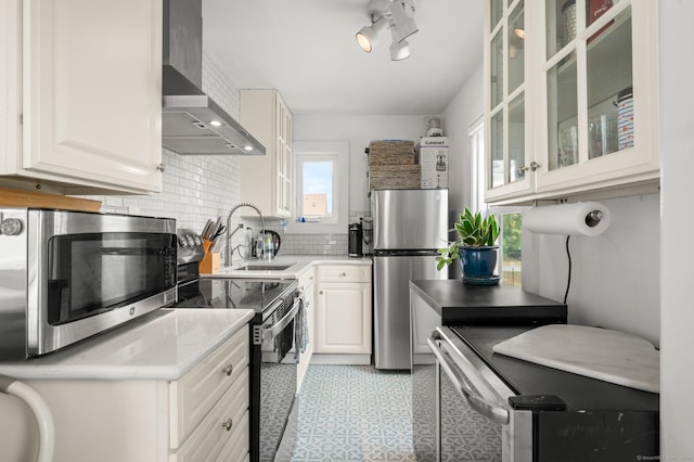 kitchen featuring appliances with stainless steel finishes, white cabinetry, sink, backsplash, and wall chimney range hood