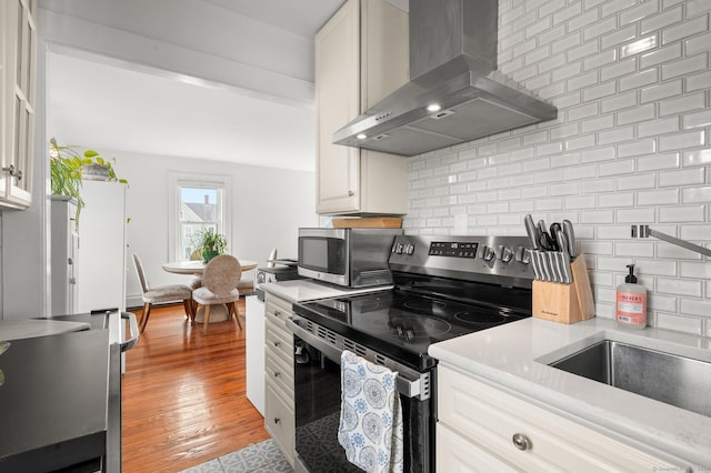 kitchen featuring appliances with stainless steel finishes, white cabinets, backsplash, exhaust hood, and light hardwood / wood-style flooring