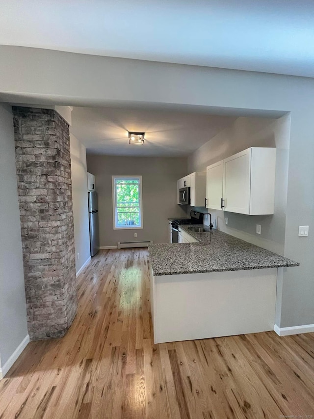 kitchen featuring appliances with stainless steel finishes, white cabinetry, dark stone countertops, baseboard heating, and kitchen peninsula