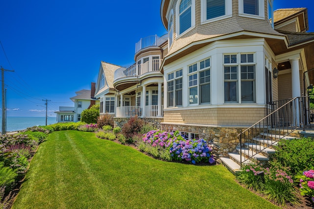 exterior space with a water view, a balcony, and a front lawn