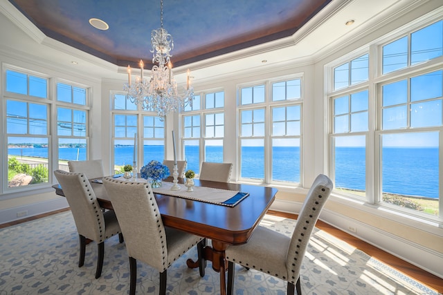 dining area featuring a water view, a raised ceiling, a chandelier, and hardwood / wood-style flooring