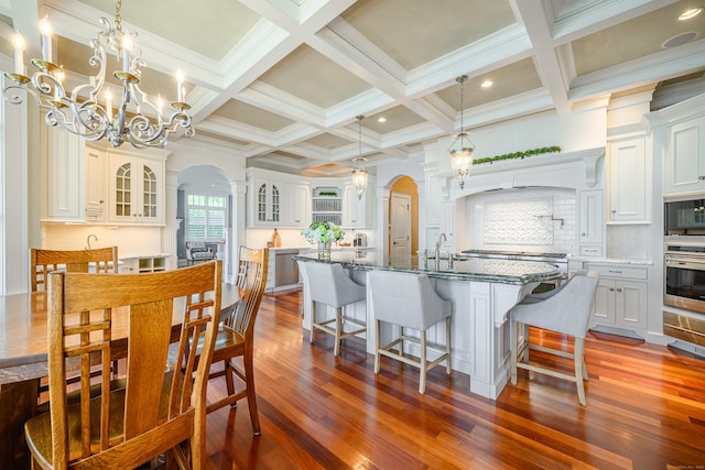 dining room with sink, hardwood / wood-style flooring, coffered ceiling, beamed ceiling, and a chandelier