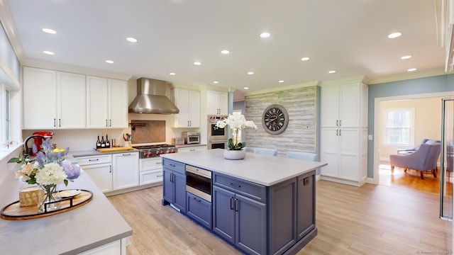 kitchen featuring wall chimney exhaust hood, white cabinetry, a center island, light wood-type flooring, and appliances with stainless steel finishes