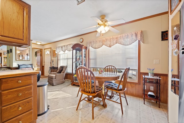 carpeted dining space featuring ornamental molding, ceiling fan, and wood walls