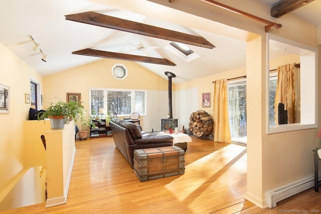 living room featuring a wood stove, rail lighting, a baseboard heating unit, lofted ceiling with beams, and light wood-type flooring