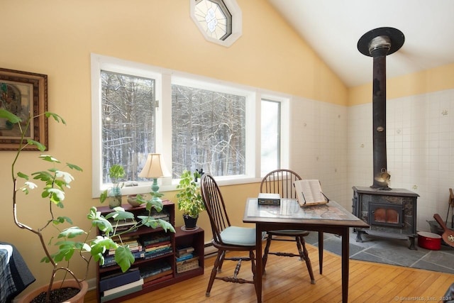 dining space with hardwood / wood-style flooring, vaulted ceiling, and a wood stove