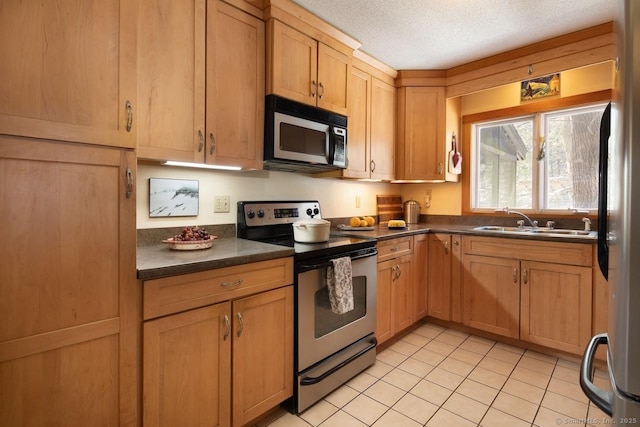 kitchen with stainless steel appliances, light tile patterned flooring, sink, and a textured ceiling