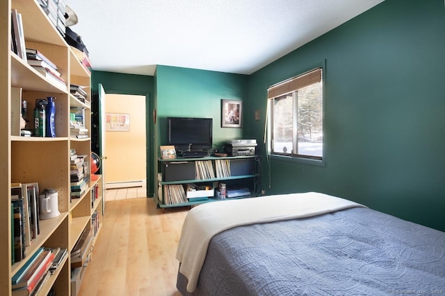 bedroom with a baseboard heating unit and light hardwood / wood-style floors