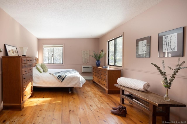 bedroom featuring light hardwood / wood-style flooring, a wall unit AC, a textured ceiling, and baseboard heating