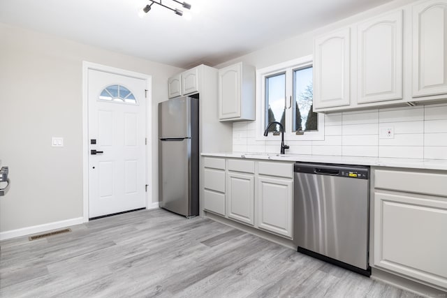 kitchen with appliances with stainless steel finishes, white cabinetry, sink, decorative backsplash, and light hardwood / wood-style floors