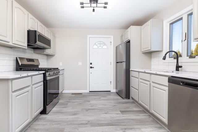 kitchen with stainless steel appliances, white cabinetry, light hardwood / wood-style floors, and decorative backsplash