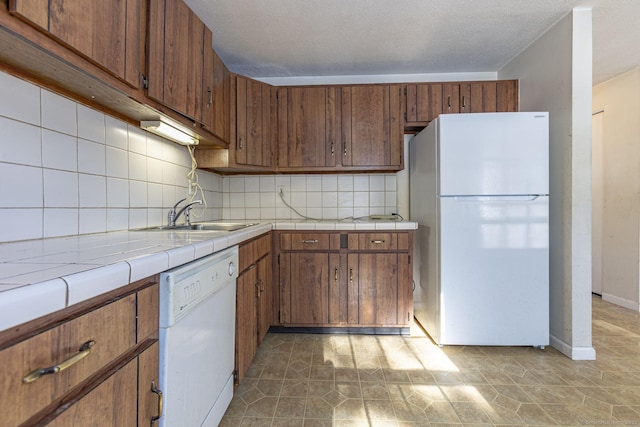 kitchen with sink, tasteful backsplash, a textured ceiling, tile counters, and white appliances