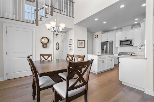 dining area with a high ceiling, sink, light hardwood / wood-style flooring, and a notable chandelier