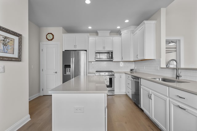 kitchen with appliances with stainless steel finishes, sink, white cabinets, a center island, and light hardwood / wood-style flooring