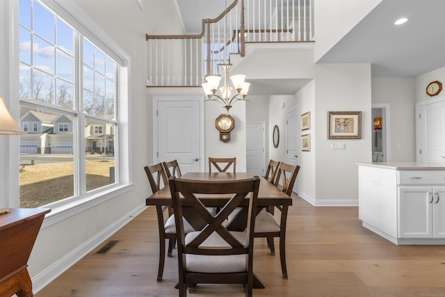 dining area with a chandelier, light hardwood / wood-style floors, and a high ceiling