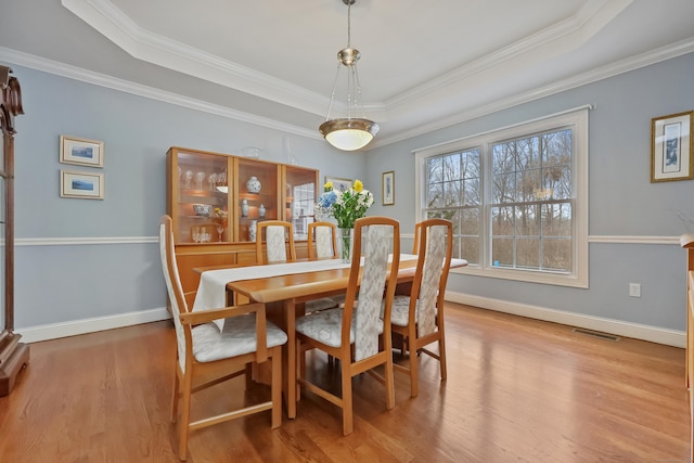 dining room featuring crown molding, a raised ceiling, and light hardwood / wood-style floors