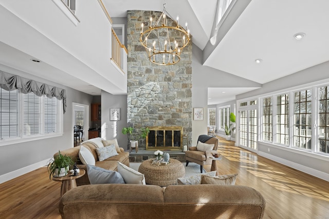 living room featuring a high ceiling, an inviting chandelier, a stone fireplace, wood finished floors, and baseboards