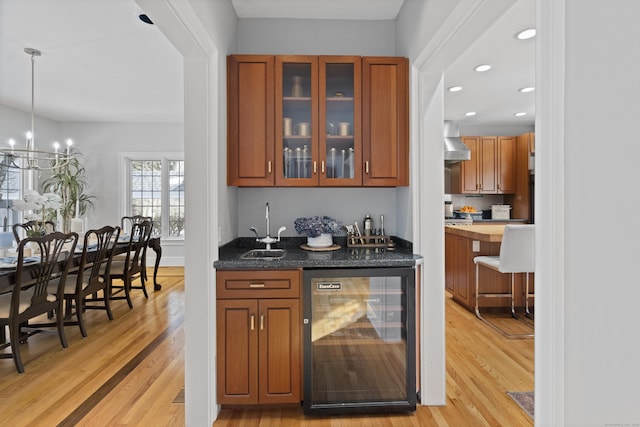 bar featuring beverage cooler, a sink, light wood-style flooring, and wall chimney range hood