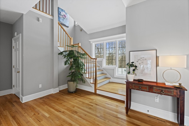 foyer entrance featuring baseboards, a high ceiling, stairway, and wood finished floors