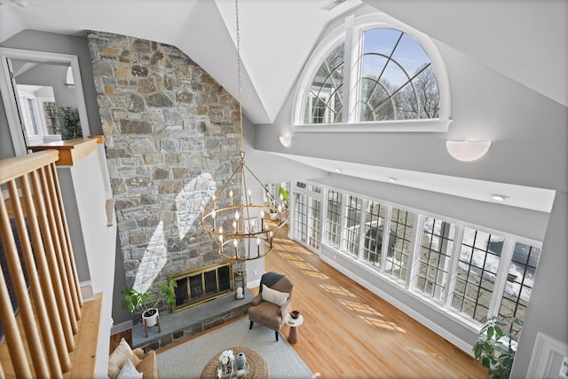 living area featuring lofted ceiling, a stone fireplace, an inviting chandelier, and wood finished floors