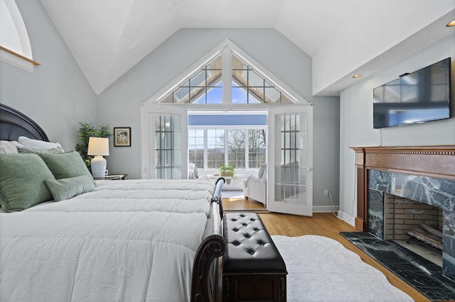 bedroom featuring vaulted ceiling, a fireplace, baseboards, and wood finished floors