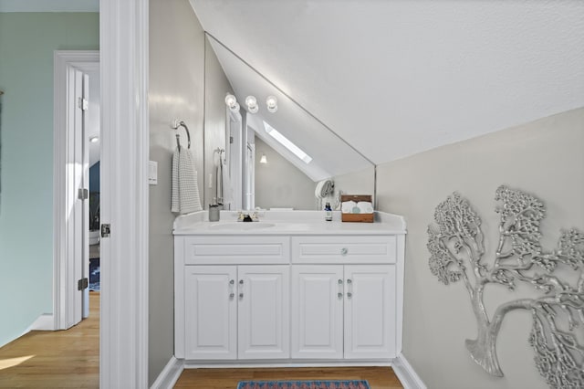 bathroom with vaulted ceiling with skylight, wood finished floors, vanity, and baseboards