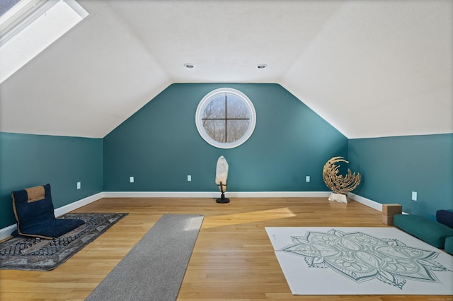 interior space featuring lofted ceiling with skylight, baseboards, and wood finished floors