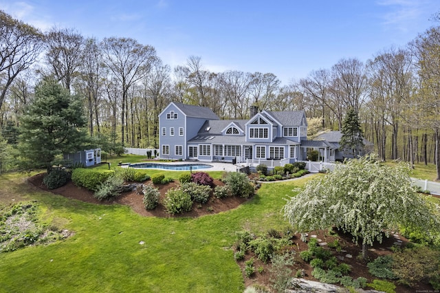 rear view of house featuring a chimney, an outdoor pool, and a yard