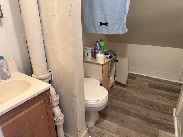 bathroom featuring vanity, wood-type flooring, lofted ceiling, and toilet