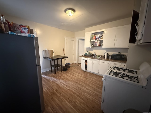 kitchen with stainless steel fridge, white gas stove, hardwood / wood-style floors, and white cabinets