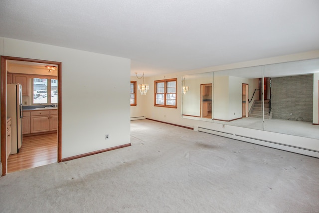 empty room featuring a baseboard radiator, a chandelier, light carpet, and a wealth of natural light