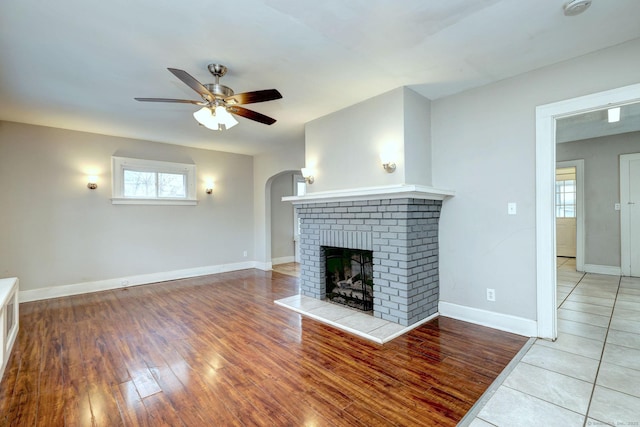 unfurnished living room featuring a brick fireplace, hardwood / wood-style flooring, and ceiling fan