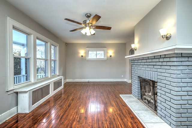 unfurnished living room featuring a brick fireplace, dark wood-type flooring, and ceiling fan