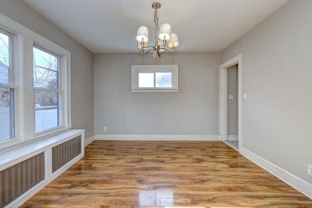 unfurnished dining area with radiator heating unit, a notable chandelier, and light hardwood / wood-style floors