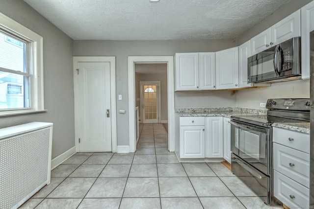 kitchen featuring radiator, black appliances, white cabinets, and light tile patterned flooring