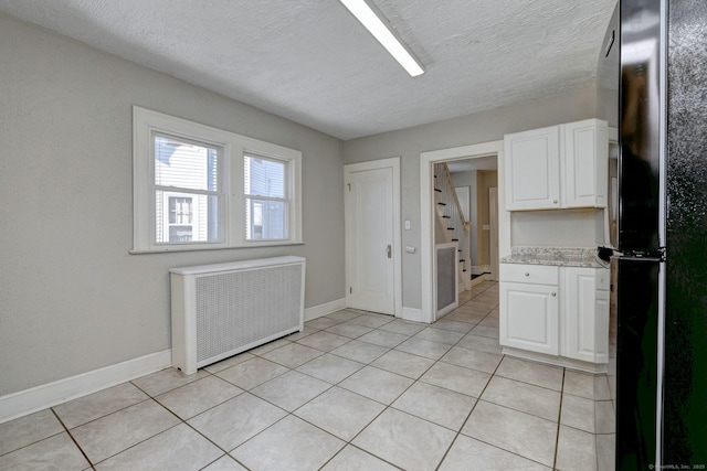 kitchen with black refrigerator, radiator, white cabinetry, and light tile patterned floors