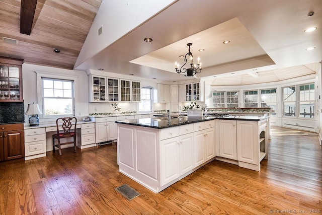 kitchen with a raised ceiling, a center island, white cabinets, and light wood-type flooring