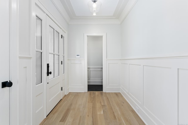 hall with ornamental molding, light wood-style flooring, a decorative wall, and a wainscoted wall