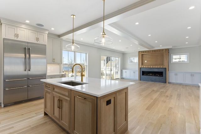 kitchen with sink, built in refrigerator, hanging light fixtures, a center island with sink, and light hardwood / wood-style flooring